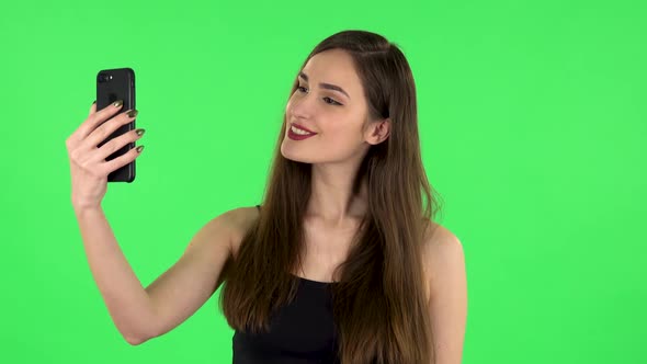 Young Woman Makes Selfie on Mobile Phone Then Looking Photos on Green Screen alt