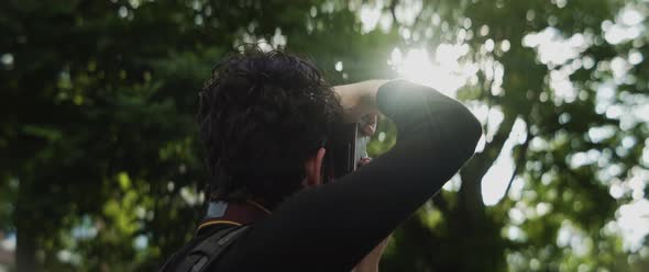 Man taking pictures of the light shining through the trees alt