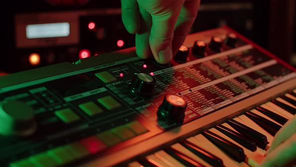 slow motion shot of a man playing keys and turning filter knobs on a vintage synth, red and green mo alt
