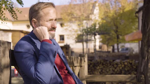 A Middleaged Caucasian Man Works on a Smartphone Then Smiles at the Camera As He Sits on a Bench