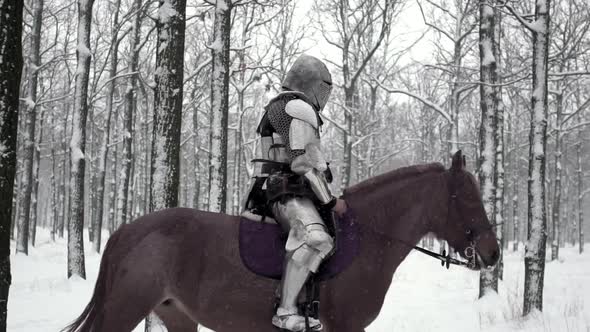 Lone Medieval Soldier Armed with Steel Weapon Riding on Dark Horse Through Winter Forest Under alt