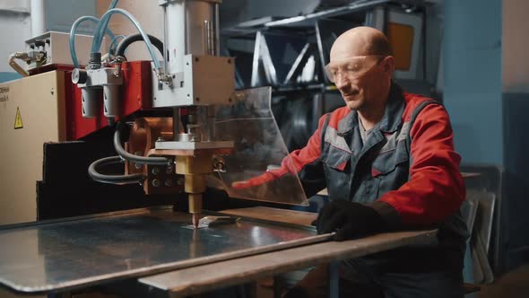 A Professional Engineer Works with a Sheet of Metal Behind a Protective Screen alt