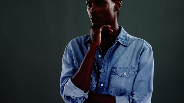 Androgynous man in denim shirt posing against dark background alt