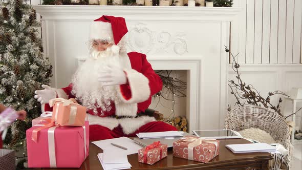 Busy Santa Sorting Chidlren's Letters While Cute Little Helper Bringing Him a Gift alt
