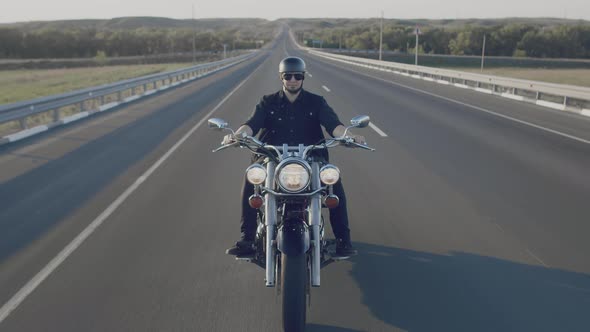 Biker in Black Glasses and Helmet Confidently Rides Along Highway on Motorcycle with Its Headlights alt