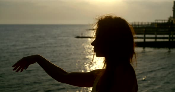 Woman Is Dancing By Hands Against Amazing Sunset Over Ocean, Silhouette of Her Body alt