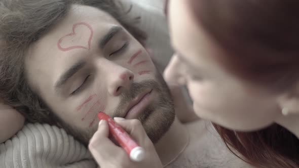 Girl Draws on the Face of a Guy Lying in Bed. Slow Motion alt