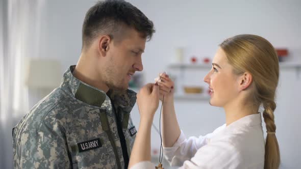 Smiling Wife Wearing Wooden Cross Necklace on Male Soldier alt