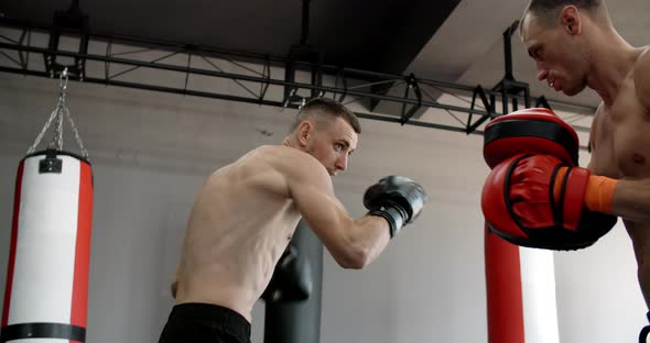 Low Angle Shot Fighter in Boxer Gloves is Practising His Strikes with Trainer in Slow Motion in the alt