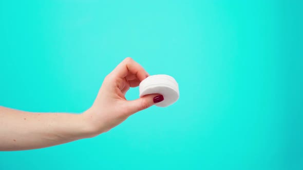 Female Hand Holding Cosmetic Cotton Discs Against Blue Background alt
