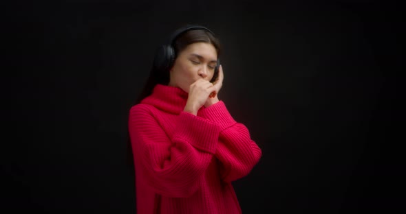 Woman Listens to Music in Wireless Headphones Smokes Vape on a Black Background