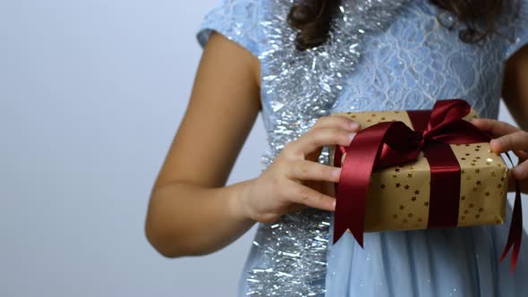 A girl in a fancy dress is holding a Christmas present. A child waiting for a gift.