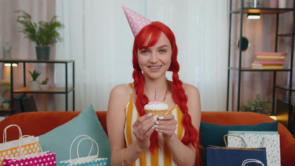 Happy Redhead Girl Celebrating Birthday Anniversary Party Blowing Candle on Small Cake Cupcake Home alt