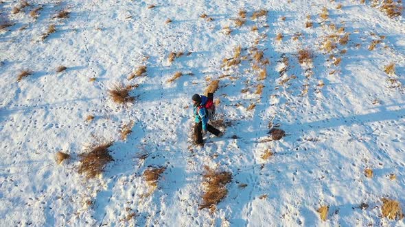 A Lone Hiker Walks Across an Endless Snowy Field. Travel Concept in Extreme Conditions. Aerial Top alt