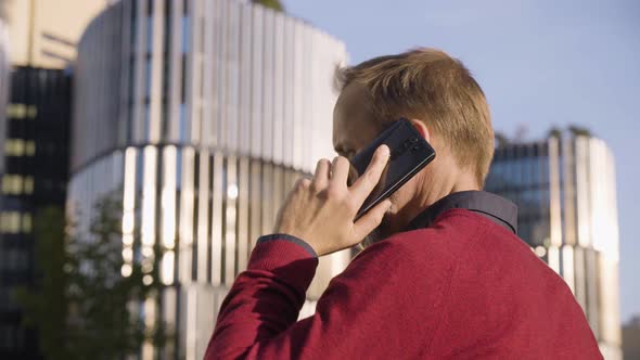 A Middleaged Handsome Caucasian Man Talks on a Smartphone with His Back to the Camera in a Street alt