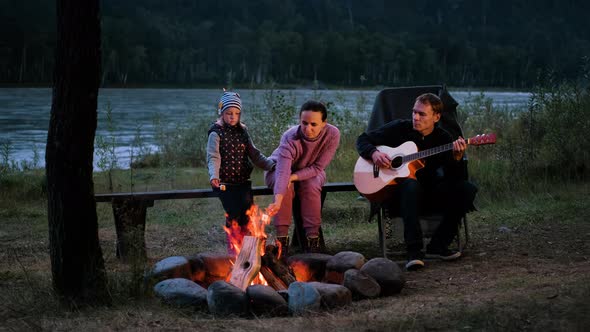 Family of Three Enjoying Vacation By the Campfire alt