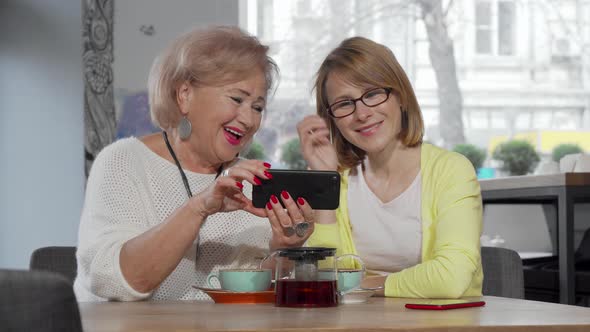 Mature Woman and Her Senior Mother Using Smart Phone at the Cafe Together alt