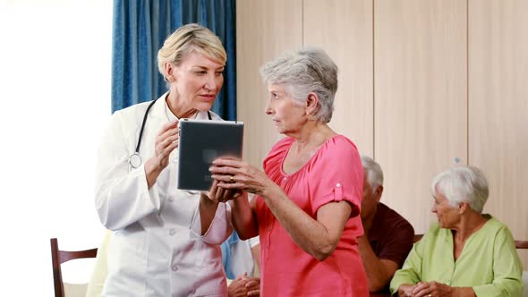 Female doctor assisting senior woman on digital tablet alt