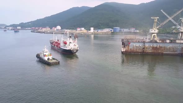 Zooming Out Freight Ship and Tugboat Drifting By Pier alt