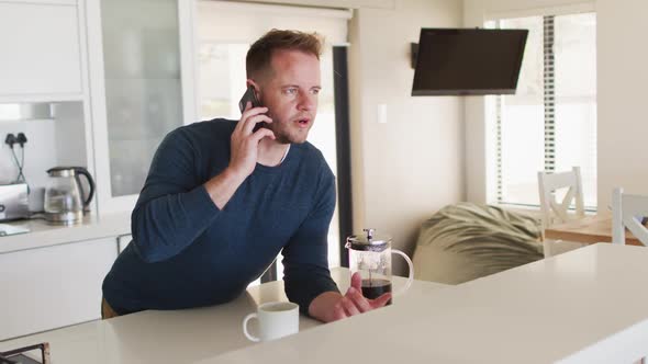 Caucasian man talking on a smartphone in kitchen alt