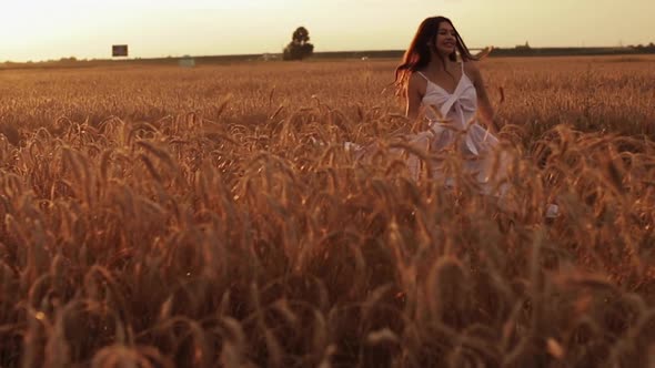 Beautiful Young Woman Enjoys Life Walking on a Wheat Field at Sunset