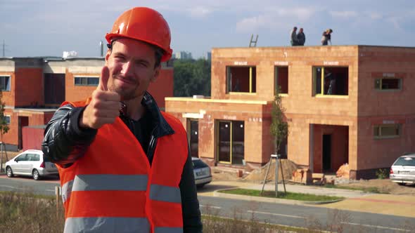 A Young Construction Worker Smiles and Shows a Thumb Up To the Camera alt