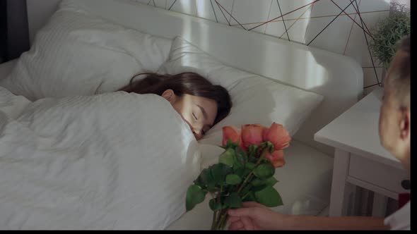Young Female Woman Sleeping in Bed and Loving Man Putting Bunch Roses on Sheet alt