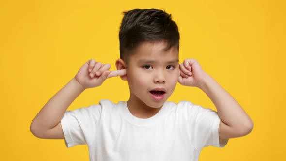 Naughty Asian Little Boy Covering Ears Shaking Head Yellow Background alt