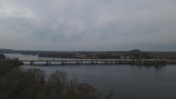 Fast paced view of traffic on bridge over river on a stormy day. Utility plant across the river.