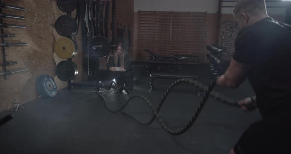Girl Taking Photos of Her Muscular Boyfriend Doing the Battle Rope Workout alt
