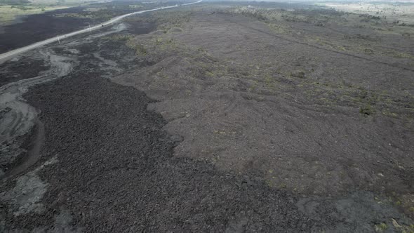 Aerial flyover dried lava field and asphalt highway in rural area of Hawaii Island. alt