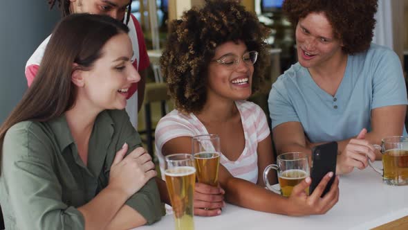 Diverse group of happy friends drinking beers and using smartphone at a bar alt