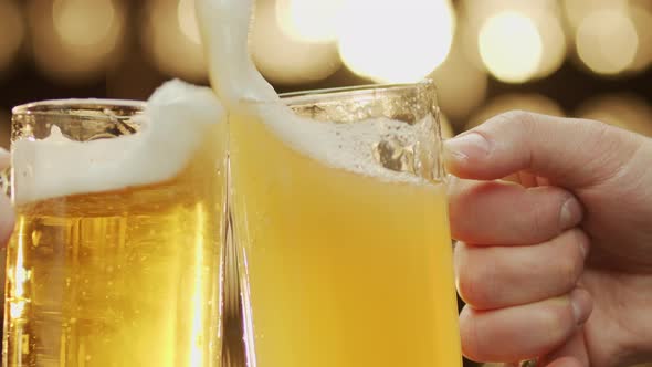 Close-up shot of two hands clinc beer spilling beer bokeh background