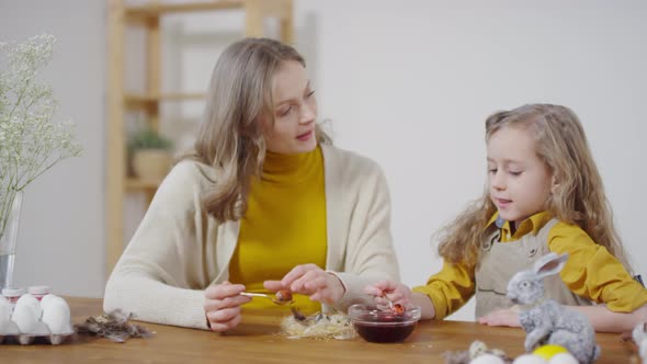 Caring Mother and Little Girl Dyeing Eggs for Easter alt