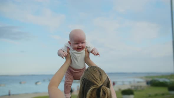 Mother Holding Up Baby Girl At Seaside alt