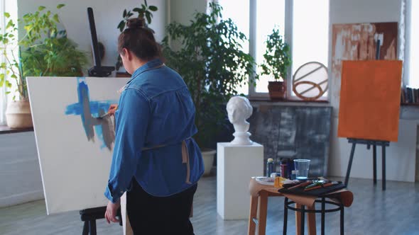 A Woman Paint Artist Drawing on a Colored Sketch on the Canvas with Blue and Grey Paint alt