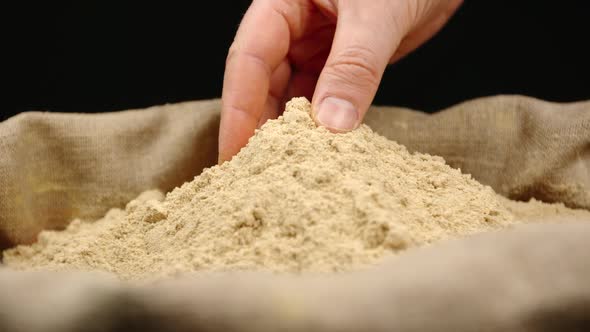 Human hand takes a pinch of a ginger powder from a top of pile in a sac