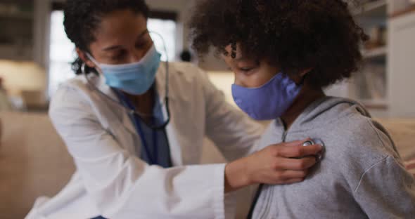 Mixed race female doctor wearing mask examining mixed race girl at home alt