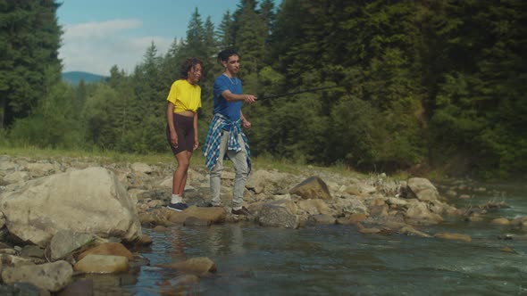 Positive Arab Man Teaching Lovely African American Woman to Fish on Mountain River alt