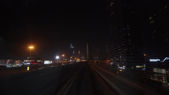 Dubai Metro Train Driving Past Skyscrapers in Urban City Center at Night alt