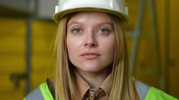 Headshot Portrait of Serious Young Woman in Hard Hat Looking at Camera Standing Indoors alt
