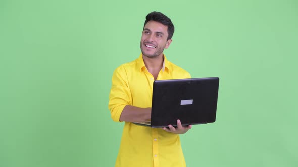 Happy Young Hispanic Businessman Thinking While Using Laptop alt