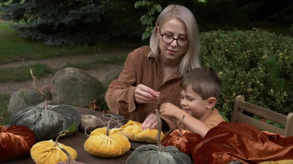 mother with son make pumpkins made of fabric on wooden table in garden