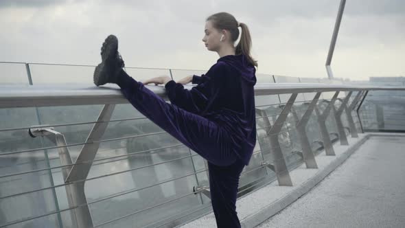 Camera Approaches To Slim Fit Sportswoman Raising Leg and Stretching on Bridge alt