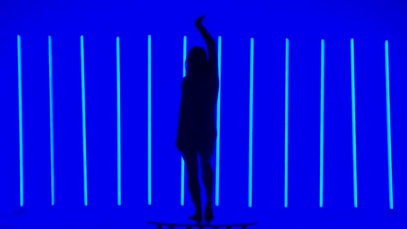 A Slim Athletic Woman Gracefully Moves Against the Backdrop of Bright Multicolored Neon Tubes alt