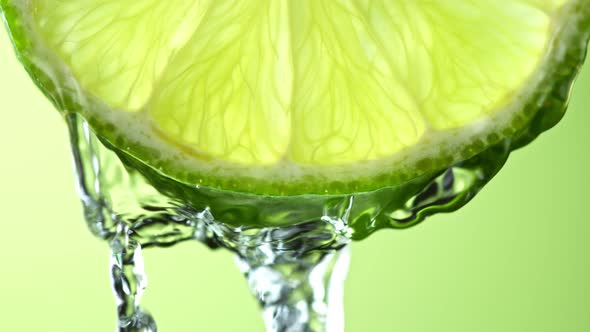 Super Slow Motion Macro Shot of Flowing Water From Lime Slice on Green Background at 1000Fps alt