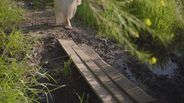 Unrecognized Woman with Bare Legs and Flowers in Hands Going Through the Small Old Bridge alt