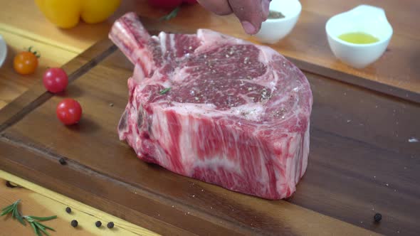 Chef cook season fresh chunk of deli piece of beef with sea salt and grounded spicy peppers.