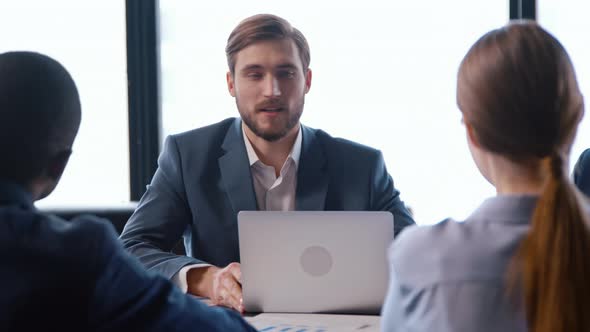 Caucasian young man in a suit talking with colleagues at a business meeting alt