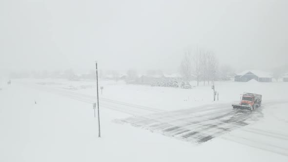 Snowplow trying to clear a highway intersection during a snowstorm with vehicles passing through.